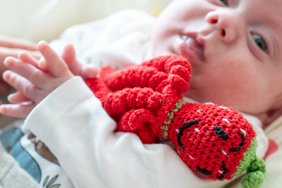 Ein Baby hält eine rote gehäkelte Krake in den Armen.